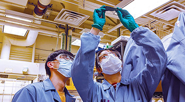 two lab workers in masks holding a piece of material aloft